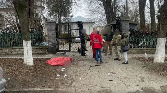 Люди біля металевих воріт будинку й червоне накриття на землі