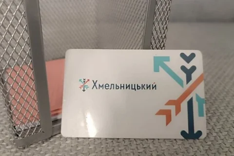 Біла пластикова транспортна картка Хмельницького зі стрілками біля металевої сітки