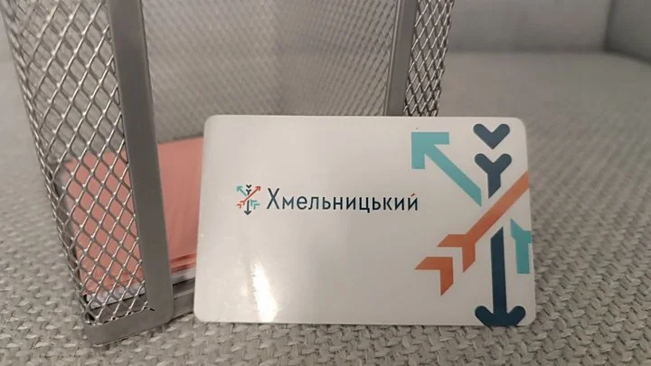 Біла пластикова транспортна картка Хмельницького зі стрілками біля металевої сітки
